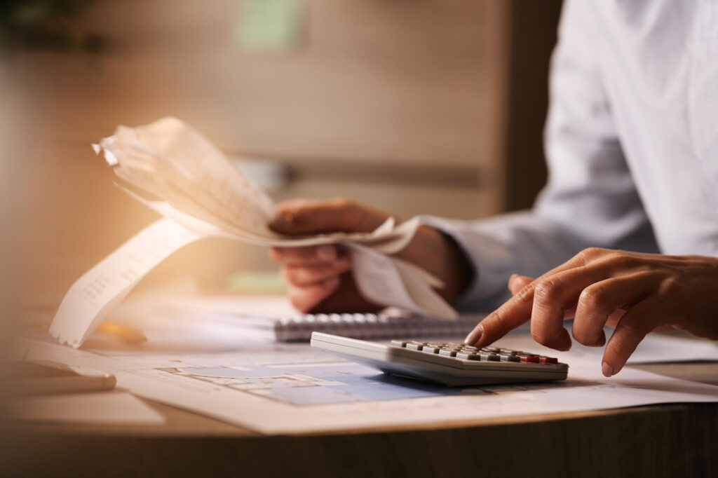 Closeup accountant using calculator while going through bills and taxes at an office sitting at a desk