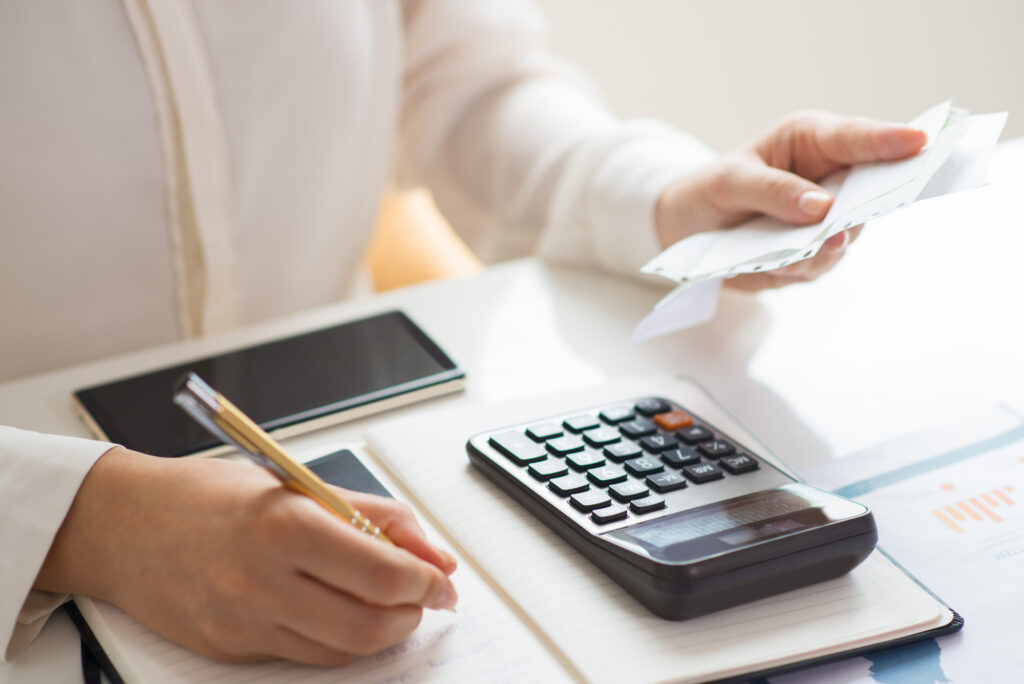 Person holding bills calculating them using a pen and calculator sitting at a desk